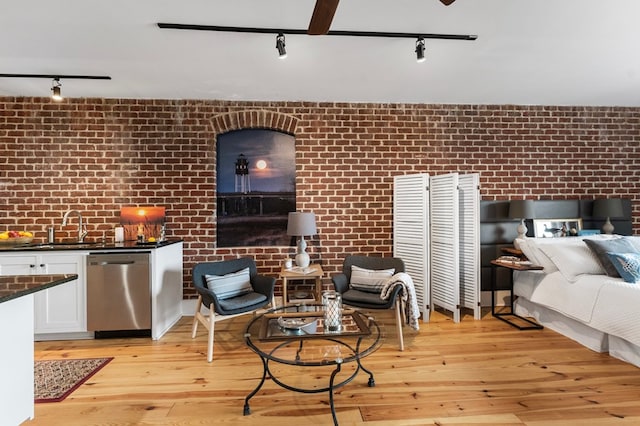 living area with brick wall, light wood-style flooring, and track lighting