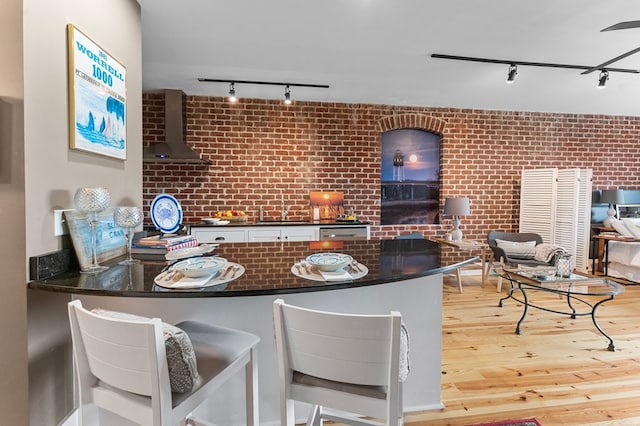 kitchen with light hardwood / wood-style flooring, rail lighting, brick wall, kitchen peninsula, and wall chimney exhaust hood