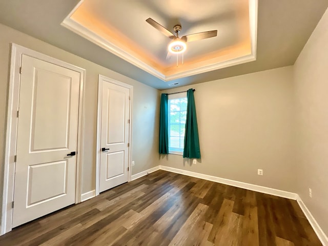 unfurnished bedroom with a tray ceiling, ceiling fan, and dark wood-type flooring