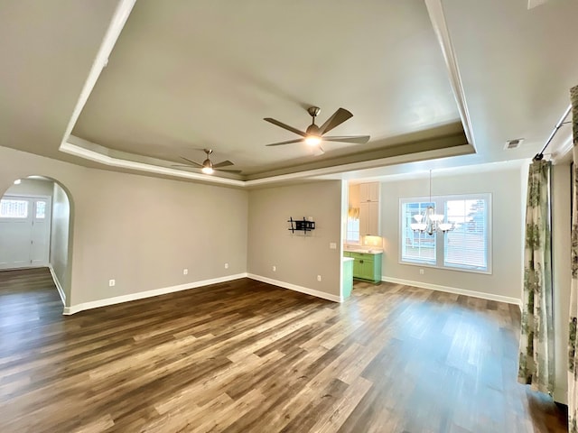 unfurnished living room with ceiling fan with notable chandelier, a tray ceiling, and dark hardwood / wood-style floors