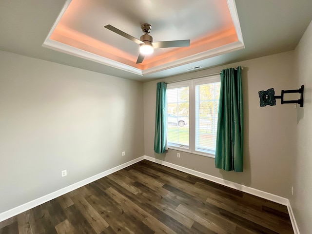 spare room with a raised ceiling, ceiling fan, and dark hardwood / wood-style flooring