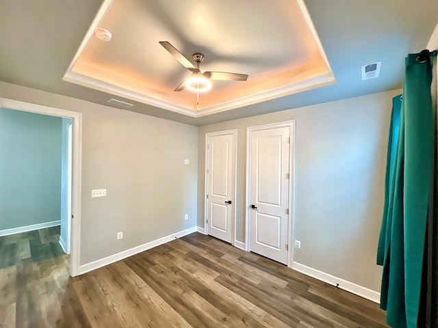 unfurnished bedroom featuring ceiling fan, dark hardwood / wood-style floors, and a raised ceiling