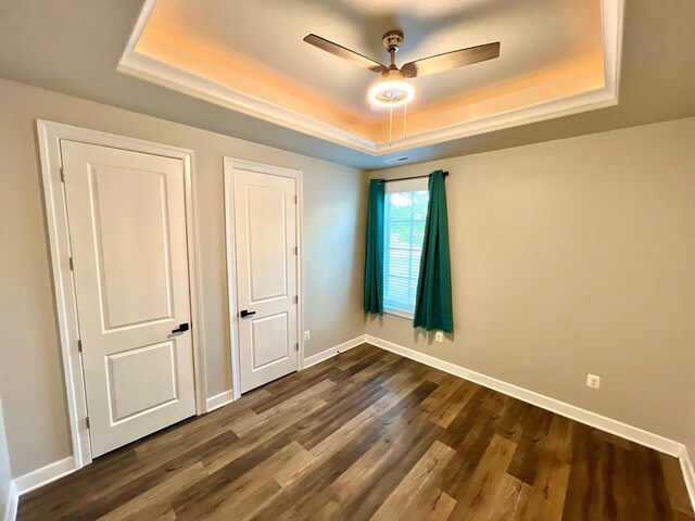 unfurnished bedroom featuring dark hardwood / wood-style flooring, a raised ceiling, and ceiling fan