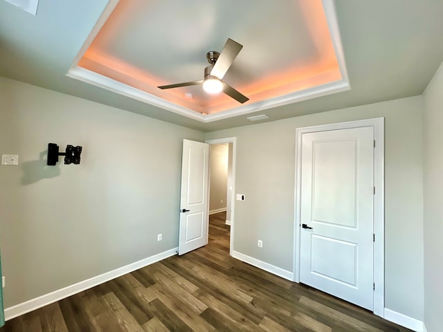 unfurnished bedroom featuring ceiling fan, dark hardwood / wood-style floors, and a tray ceiling