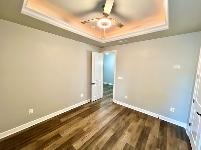 unfurnished bedroom featuring a tray ceiling, ceiling fan, and dark hardwood / wood-style floors