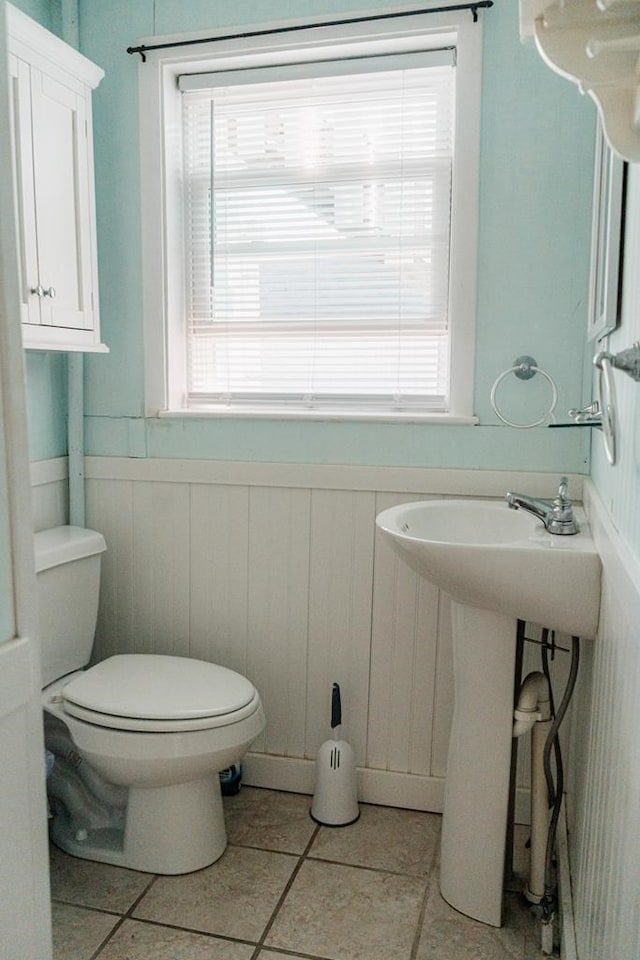 half bath with wainscoting, toilet, and tile patterned floors