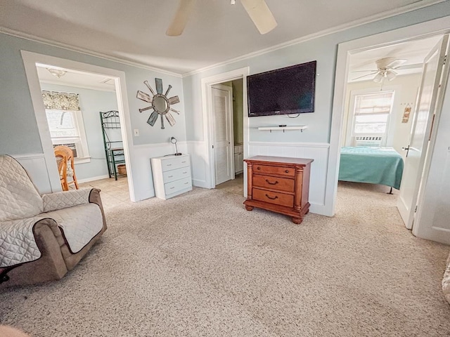 living area with a wainscoted wall, ornamental molding, a ceiling fan, and light colored carpet