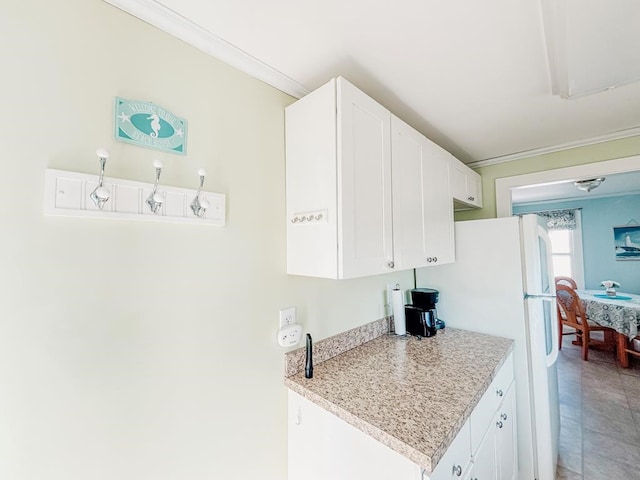 kitchen with freestanding refrigerator, light countertops, ornamental molding, and white cabinetry