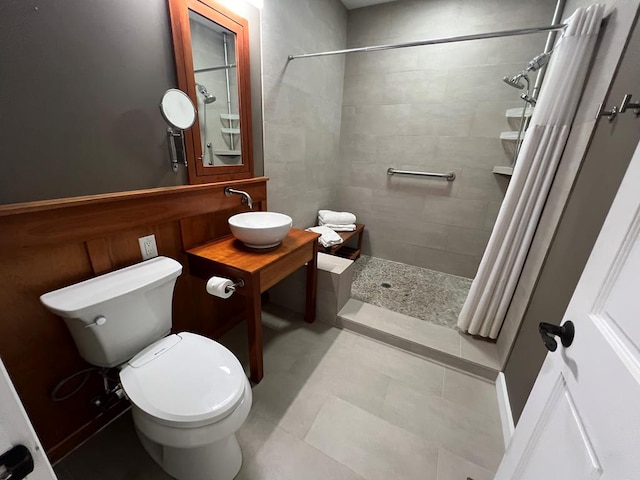 full bath featuring a tile shower, toilet, and a sink
