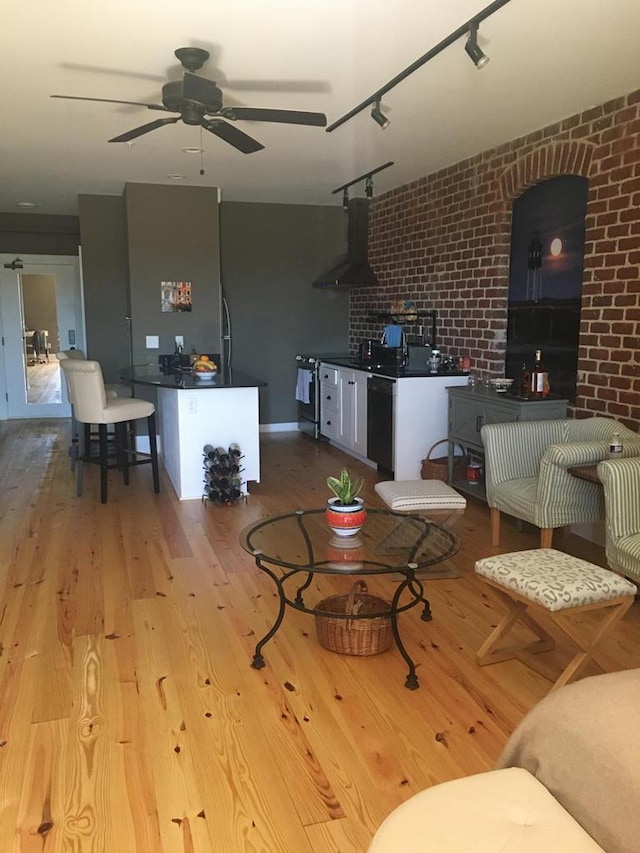 living room with wood finished floors, ceiling fan, and brick wall