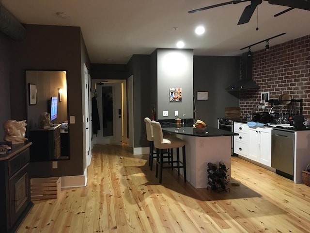 kitchen featuring stainless steel appliances, light wood-style floors, rail lighting, wall chimney exhaust hood, and dark countertops