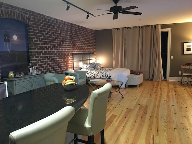 bedroom with track lighting, wood finished floors, and brick wall