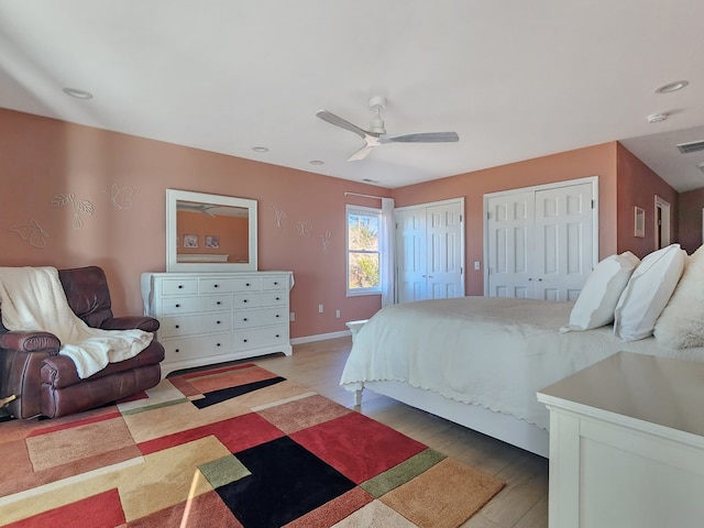 bedroom featuring ceiling fan, light wood-style flooring, visible vents, baseboards, and multiple closets