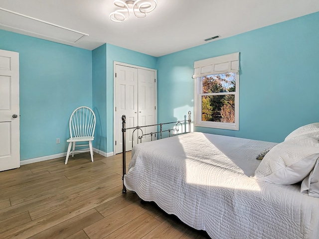 bedroom with wood finished floors, visible vents, baseboards, a closet, and attic access