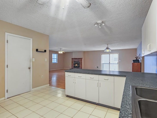 kitchen with sink, ceiling fan, a textured ceiling, a fireplace, and white cabinetry