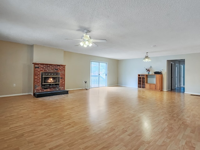 unfurnished living room featuring a brick fireplace, ceiling fan, a textured ceiling, and light hardwood / wood-style flooring