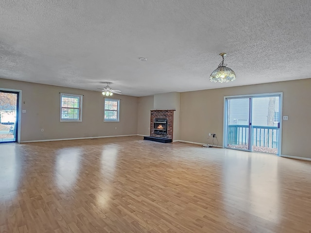 unfurnished living room featuring a fireplace, a textured ceiling, light wood-type flooring, and ceiling fan