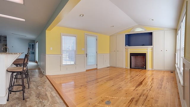 living area featuring vaulted ceiling, wainscoting, a fireplace, and light wood-style floors