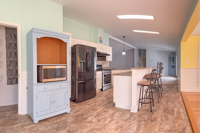 kitchen with decorative light fixtures, a breakfast bar area, stainless steel appliances, white cabinets, and under cabinet range hood