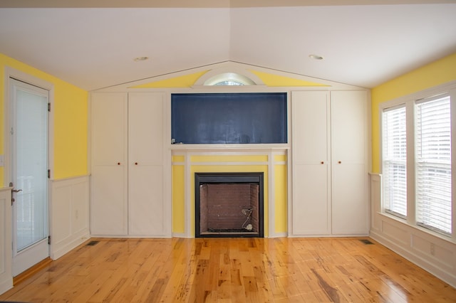 unfurnished living room featuring a fireplace, lofted ceiling, visible vents, a decorative wall, and light wood-style flooring