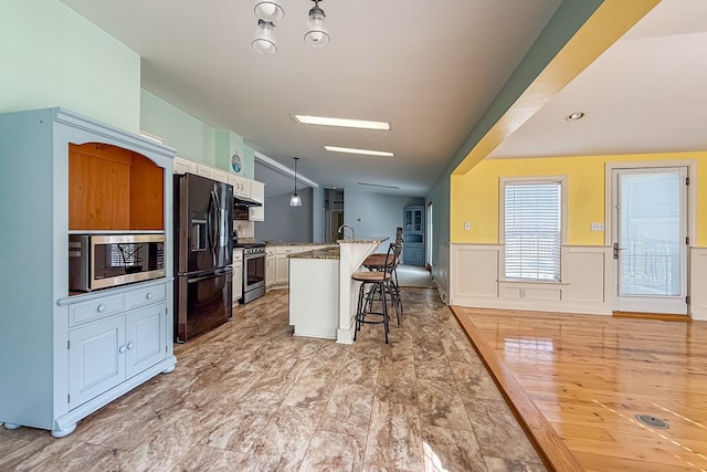 kitchen with a breakfast bar, stainless steel appliances, a kitchen island with sink, white cabinetry, and light stone countertops