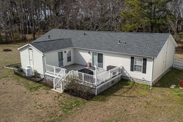 back of property featuring roof with shingles, a deck, and a yard