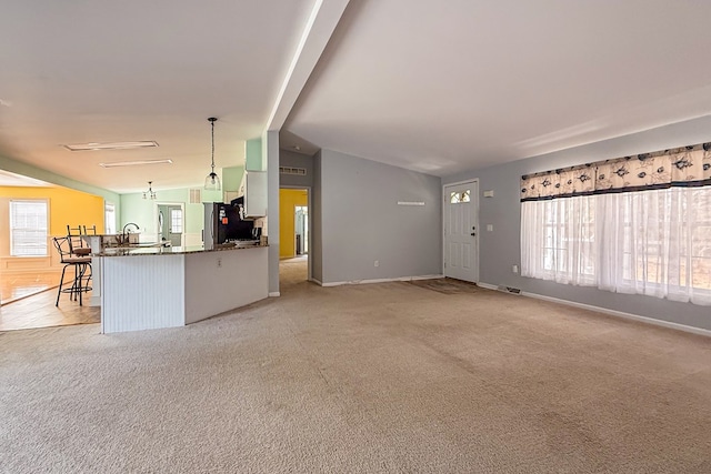 unfurnished living room featuring light colored carpet, vaulted ceiling, visible vents, and baseboards