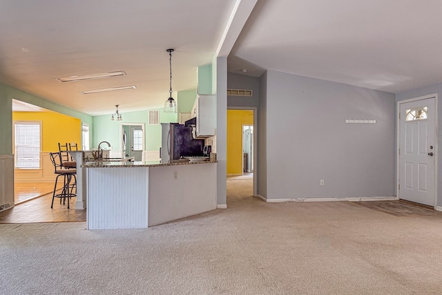 kitchen with light colored carpet, freestanding refrigerator, a kitchen bar, white cabinetry, and pendant lighting