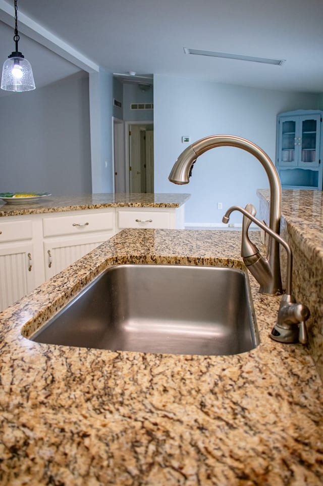 details with stone countertops, visible vents, white cabinets, hanging light fixtures, and a sink