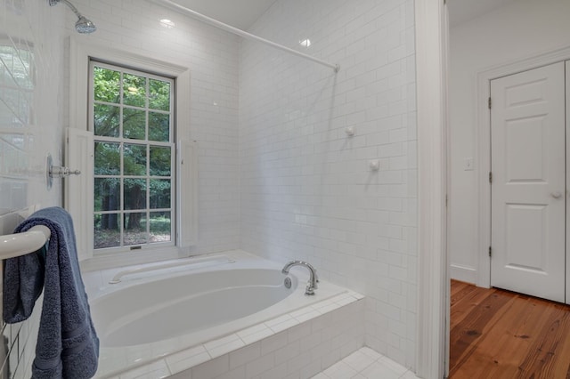 bathroom featuring a relaxing tiled tub and wood-type flooring