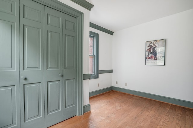 unfurnished bedroom featuring a closet, ornamental molding, and light wood-type flooring