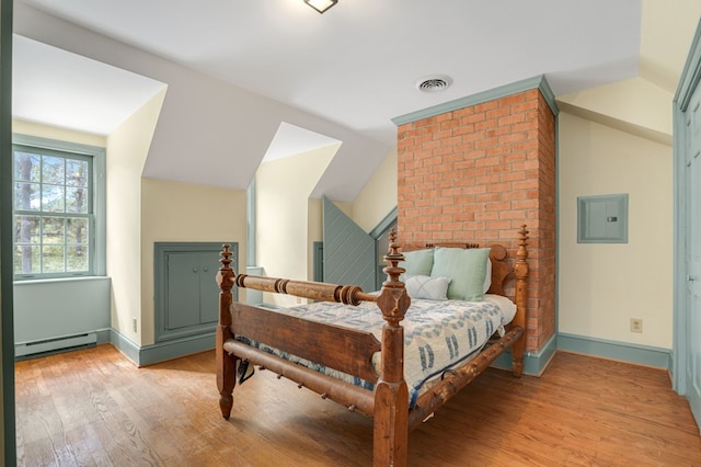 bedroom featuring electric panel, a baseboard radiator, light hardwood / wood-style floors, and vaulted ceiling