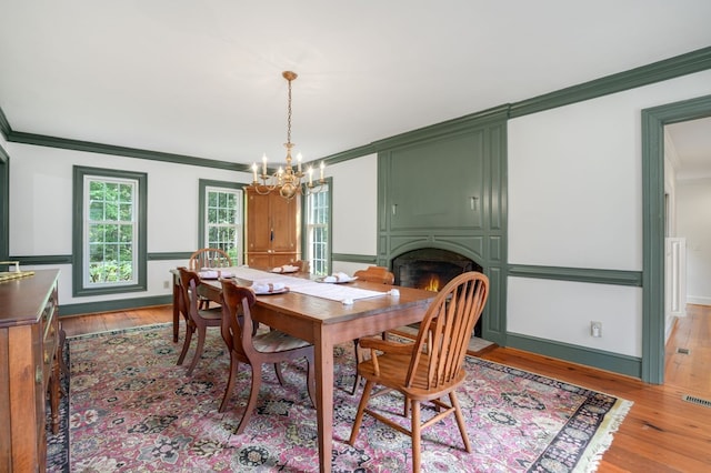 dining room with a chandelier, a large fireplace, crown molding, and light hardwood / wood-style flooring