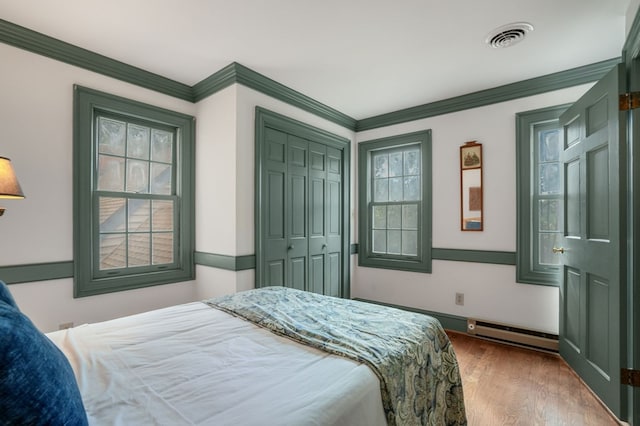 bedroom with a baseboard heating unit, wood-type flooring, ornamental molding, and a closet