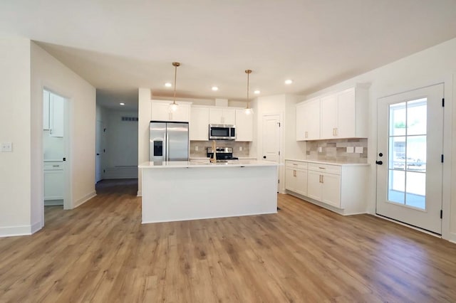 kitchen featuring white cabinetry, appliances with stainless steel finishes, hanging light fixtures, and a center island with sink