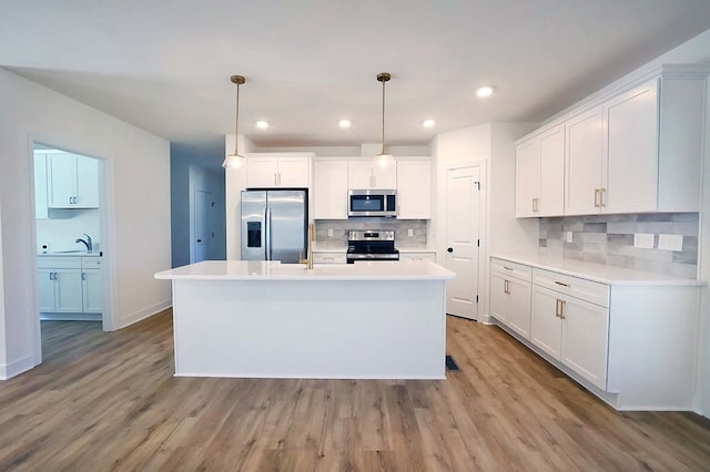 kitchen with pendant lighting, stainless steel appliances, a kitchen island with sink, and white cabinets