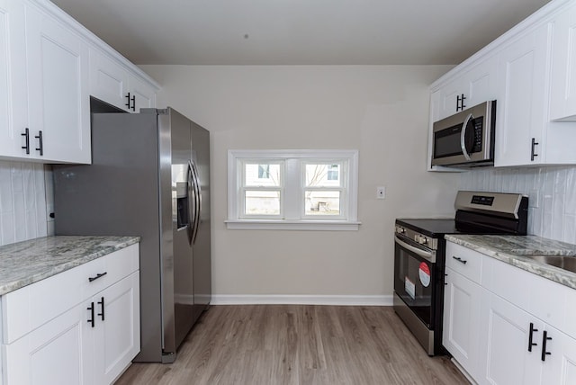 kitchen featuring appliances with stainless steel finishes, tasteful backsplash, light stone countertops, white cabinets, and light wood-type flooring