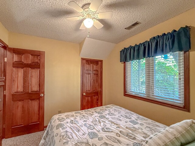 carpeted bedroom featuring vaulted ceiling, a textured ceiling, visible vents, and ceiling fan