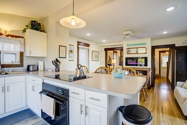 kitchen with kitchen peninsula, hanging light fixtures, white cabinets, and black appliances