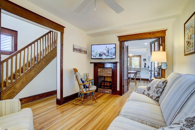 living room with a brick fireplace, ceiling fan, and light wood-type flooring