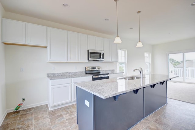 kitchen with a center island with sink, white cabinets, appliances with stainless steel finishes, pendant lighting, and a sink