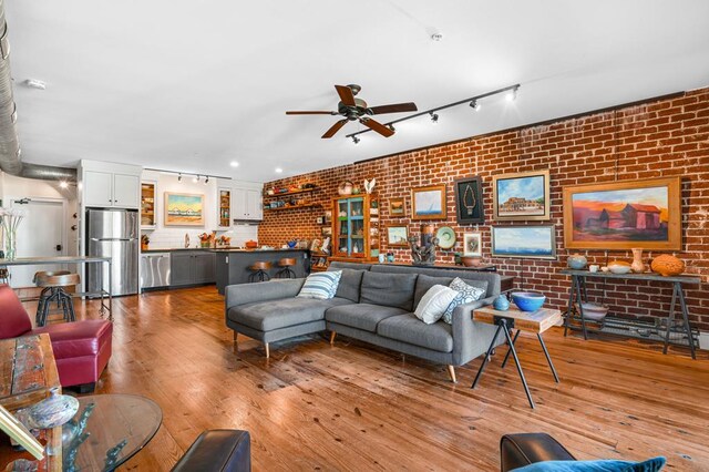 living room featuring rail lighting, brick wall, and light wood-type flooring