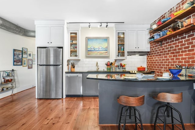 kitchen featuring appliances with stainless steel finishes, sink, light hardwood / wood-style floors, white cabinetry, and a breakfast bar area