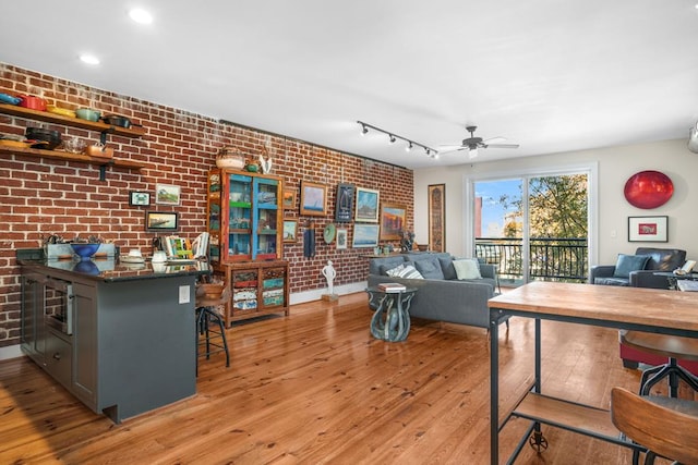 living room with light wood-type flooring, track lighting, ceiling fan, and brick wall