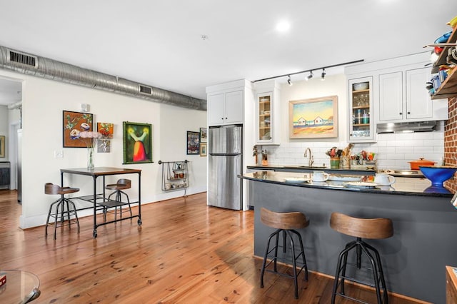 kitchen featuring a kitchen breakfast bar, stainless steel refrigerator, tasteful backsplash, and white cabinets