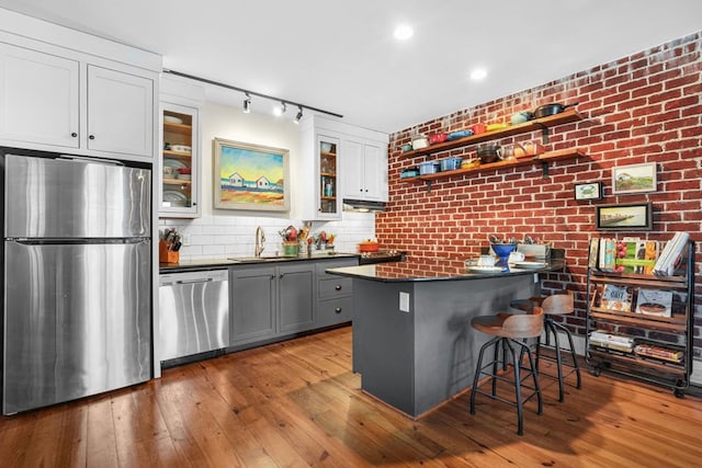 3002E Mason Ave, Cape Charles, VA 23310 - kitchen featuring appliances with stainless steel finishes, dark countertops, a breakfast bar, hardwood / wood-style floors, and brick wall