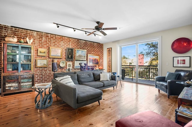 living room with ceiling fan, brick wall, track lighting, and hardwood / wood-style flooring