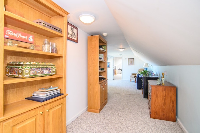 hall featuring light colored carpet, lofted ceiling, and baseboards