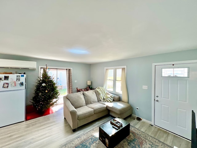 living room with light hardwood / wood-style flooring, a wall unit AC, and a healthy amount of sunlight