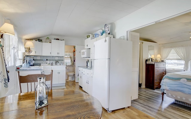 kitchen featuring white appliances, light wood finished floors, white cabinets, lofted ceiling, and light countertops